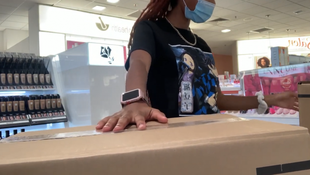 ulta's female cashier wearing a mask and with her hand on a box at the register