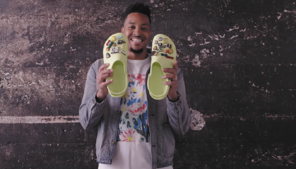 man holding a pair of Neon green crocs clogs with many Jibbitz™ attached 