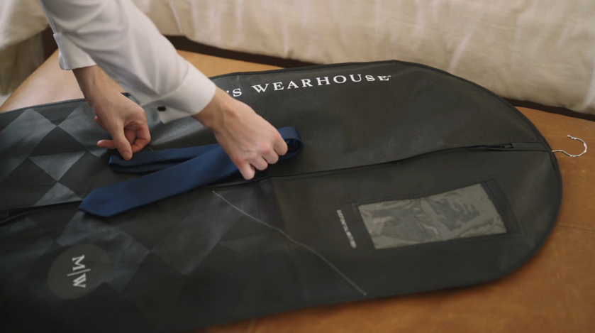 man hands putting a tie on a mens wearhouse suit cover bag