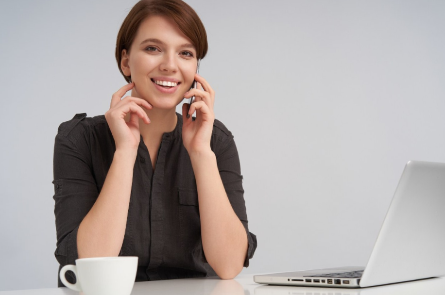 protrait of a smiling woman on a call with her laptop and coffee mug on the desk