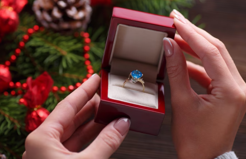 Hands holding a box with a ring with a blue stone
