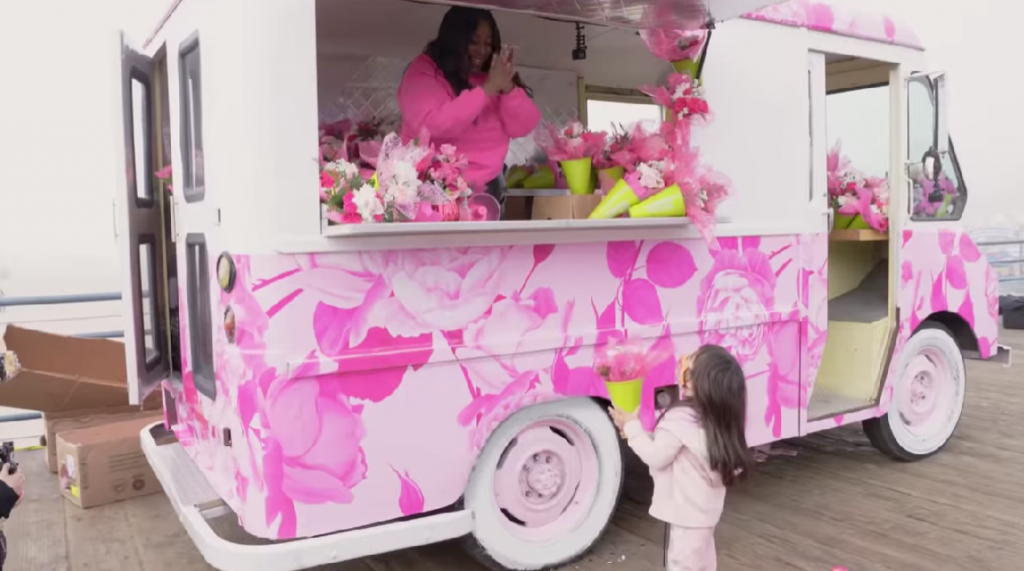 Woman of color selling flowers in a little pink truck to a little girl